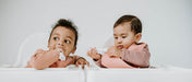 Baby boy and girl wearing Boo Chew silicone feeding bib in rust