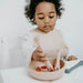 Toddler eating from silicone bowl and using silicone giraffe spoons in oat