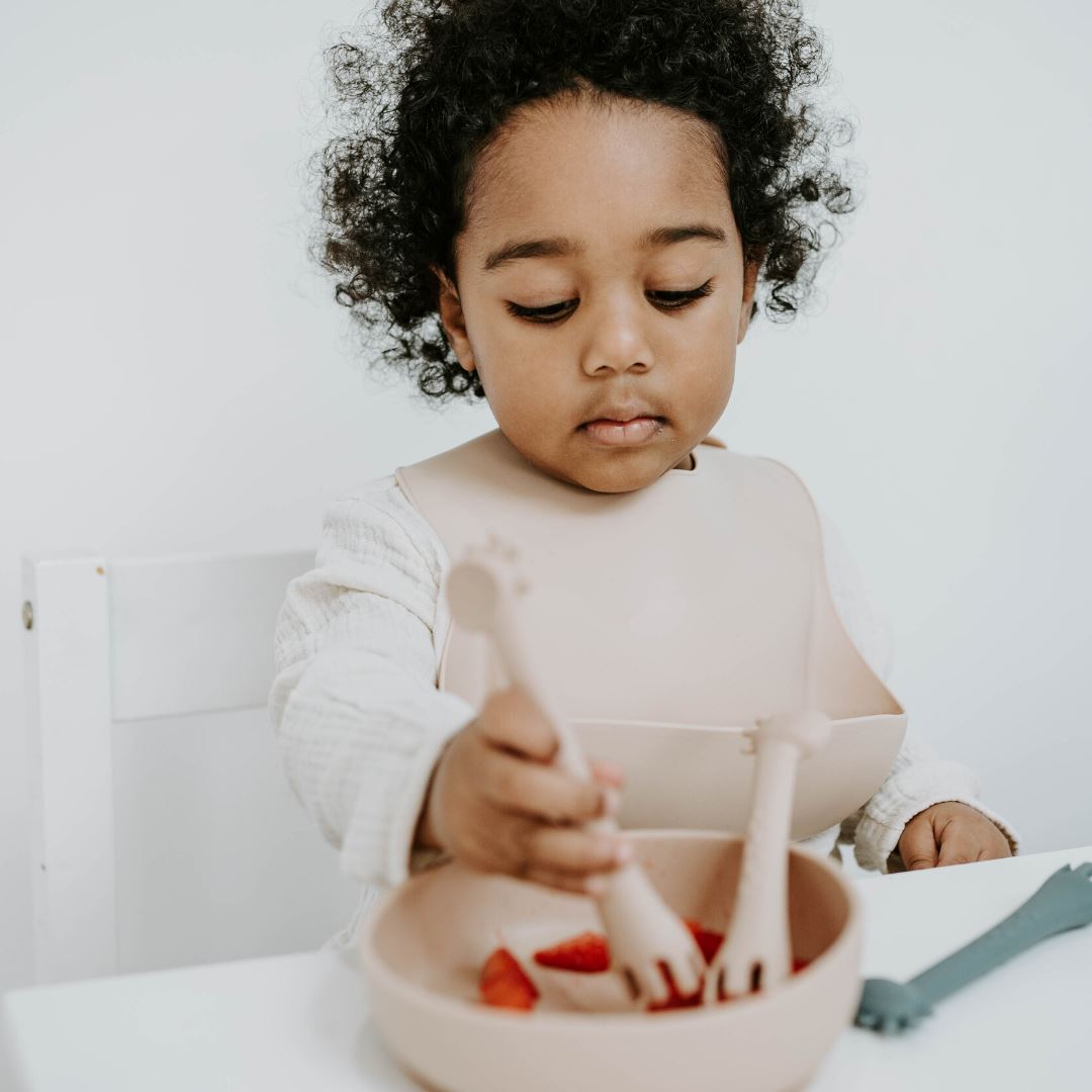 2 year old girl uses silicone giraffe 2 in 1 fork and spoon to eat strawberries