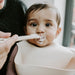 Baby sits on Mother's lap weaning, eating yoghurt from silicone giraffe spoon